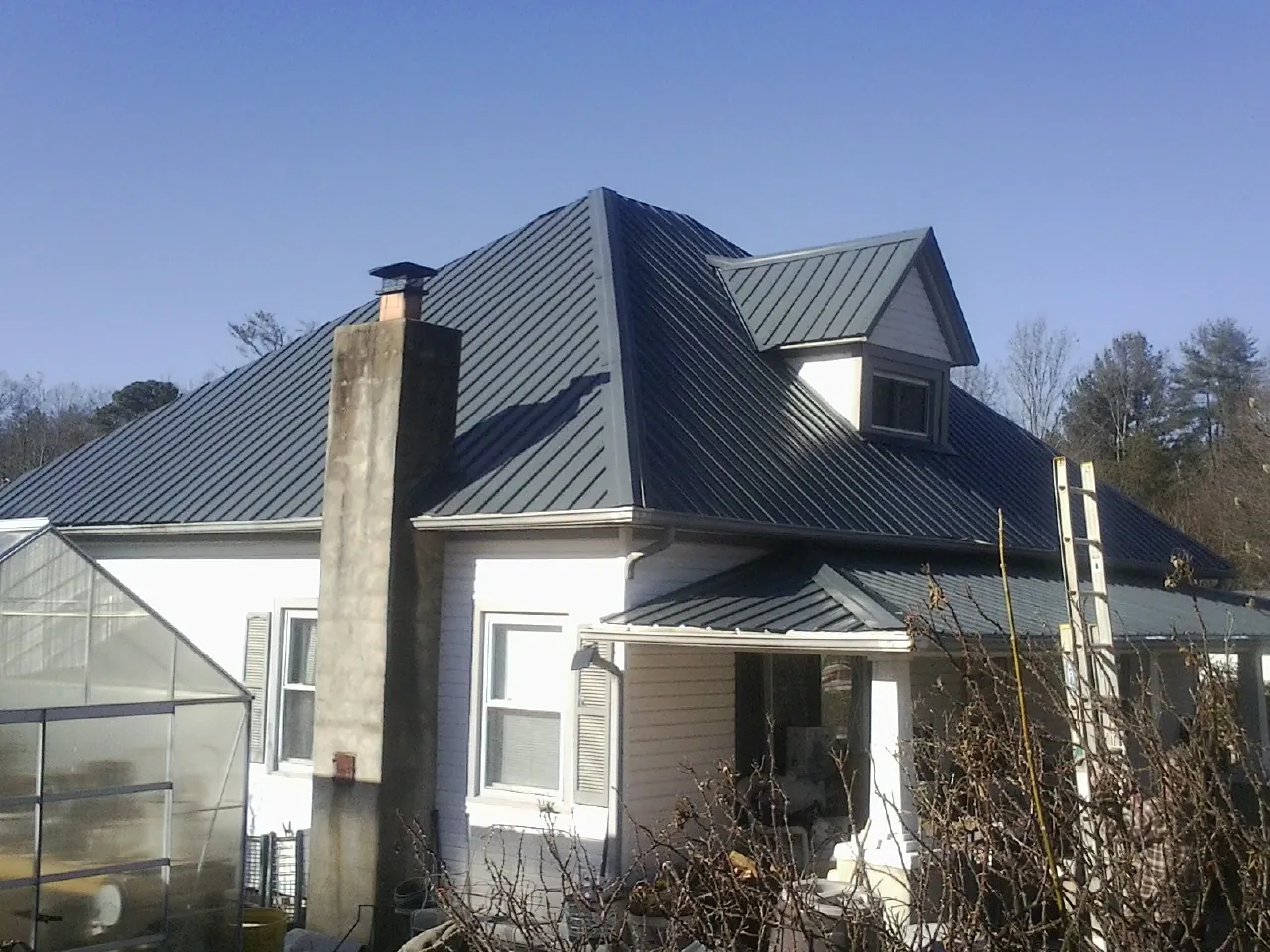 Dark blue standing seam metal roof on a white farmhouse with dormer — Slate & Tile Roof Repair by Roofing Brothers in Timberville