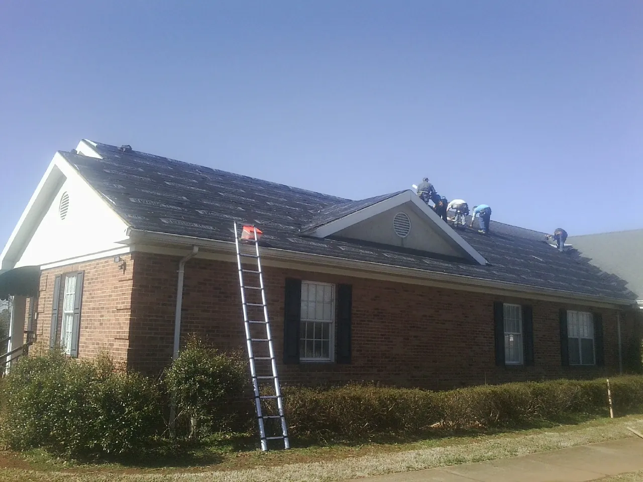 Crew tearing shingles off a brick ranch roof with a ladder set — Emergency Roof Repair work by our crew in Timberville