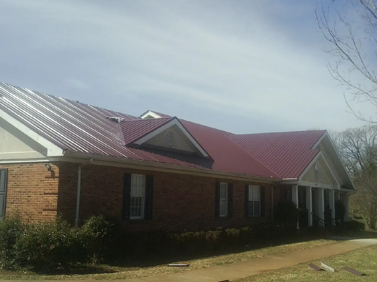 Red metal roof with gabled entries on a long brick building, from a Hail Damage Roof Repair job in Timberville