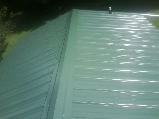 New green metal panels meeting at the ridge of a roof — Flat Roof Repair work by our crew in Timberville