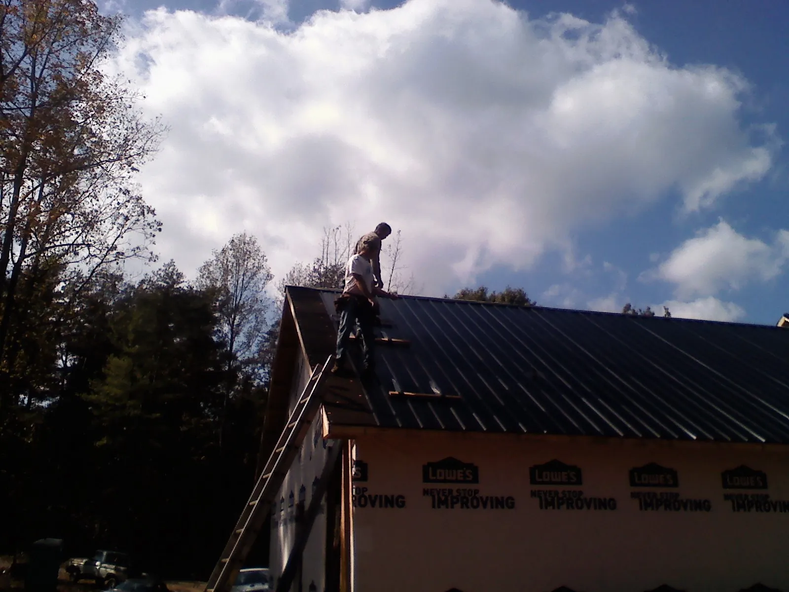 Roofer fastening dark metal panels high against a cloudy sky, from a Roof Inspection job in Timberville
