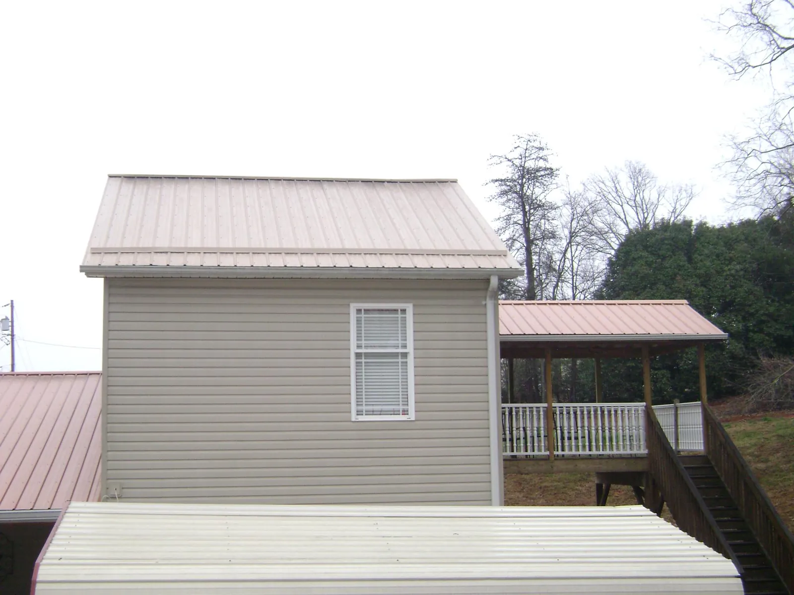 Tan metal roofs on a two story addition and attached porch, from a Roof Replacement job in Timberville
